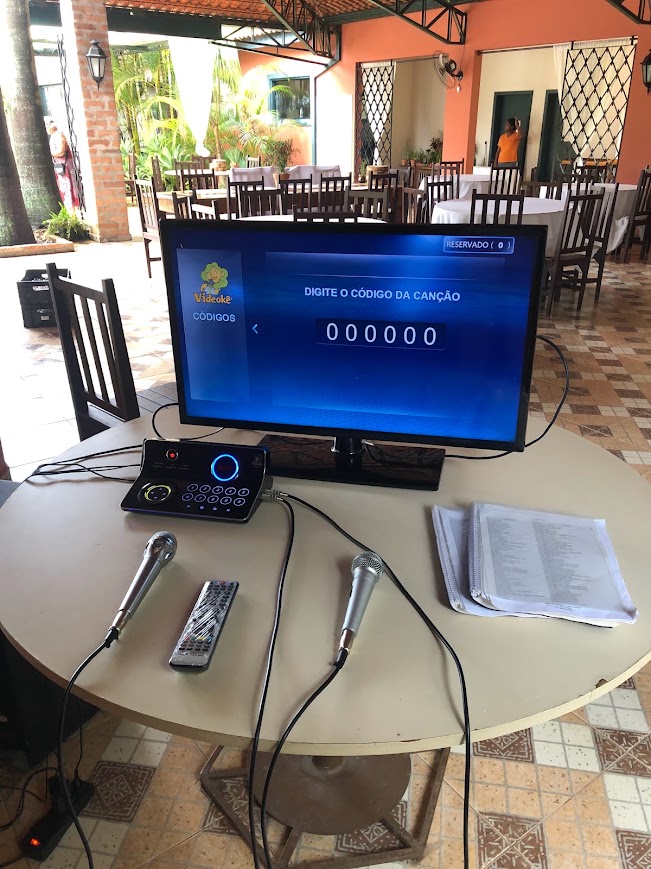 Equipamento de Videokê pronto em salão de festas com microfones e catálogo