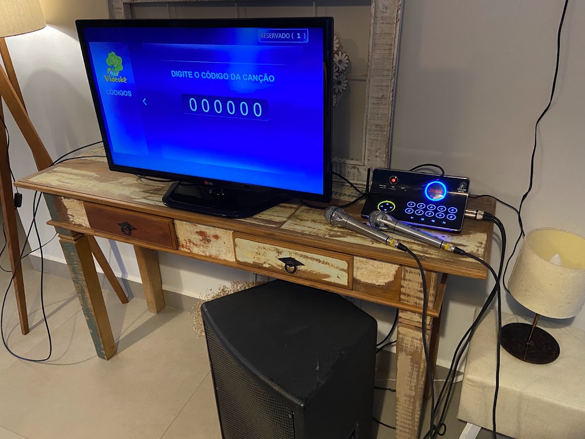 Aparelho de Videokê instalado com TV, microfones e caixa de som em sala